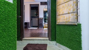 A hallway with artificial green walls, a wooden door leading to a kitchen, and a window with patterned curtains. - The Whispering Pines (Mussoorie)