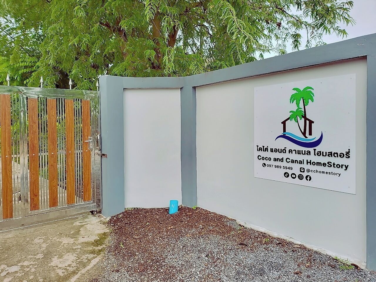 A gated entrance with a signboard displaying a logo and contact information.
