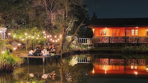 A serene lakeside setting with a wooden dock and a building with warm lighting. - Coco and Canal HomeStory (Samut Sakhon)