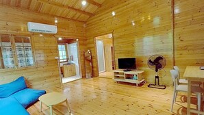 A wooden cabin interior with a sofa, TV, fan, and a small table. - Coco and Canal HomeStory (Samut Sakhon)