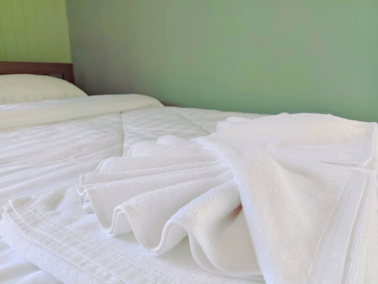 A neatly made bed with white linens and pillows, a wooden headboard, and a green wall in the background.
