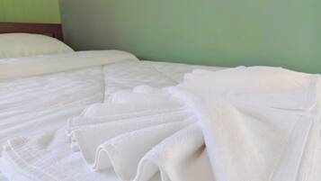 A neatly made bed with white linens and pillows, a wooden headboard, and a green wall in the background.