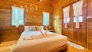 A wooden cabin bedroom with a bed, curtains, and a small table with a vase. - Coco and Canal HomeStory (Samut Sakhon)