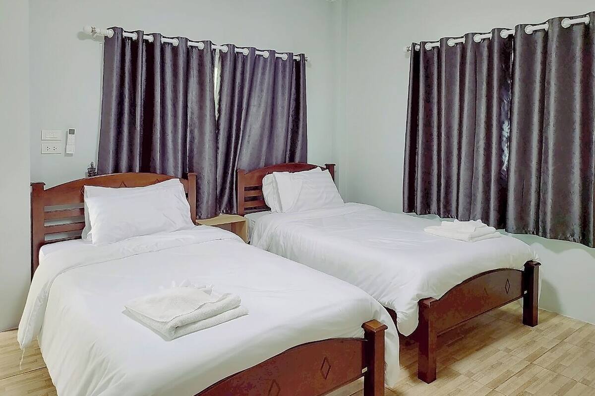 A room with two single beds, wooden headboards, white bedding, and dark curtains.