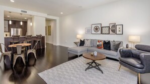 A modern living room with a gray sofa, a coffee table, and a dining area with chairs and a table. - Comfort at the Star I 2 Bed Apt in Houston (Houston)