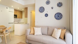 A modern living room with a beige sofa, a small dining table, and a kitchen in the background. - Elegant Urban Living by the Beach in Estepona (Estepona)
