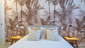 A bedroom with a bed, two nightstands, and a wall mural of tropical foliage. - Elegant Urban Living by the Beach in Estepona (Estepona)