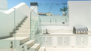 A modern outdoor kitchen with a glass staircase, a grill, and a view of the city. - Stylish Urban Escape – 2-Bedroom Apartment with Rooftop Pool (Estepona)