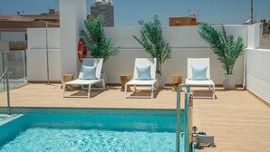 A rooftop pool area with three white lounge chairs, each with a light blue cushion, surrounded by potted plants. - Stylish Urban Escape – 2-Bedroom Apartment with Rooftop Pool (Estepona)