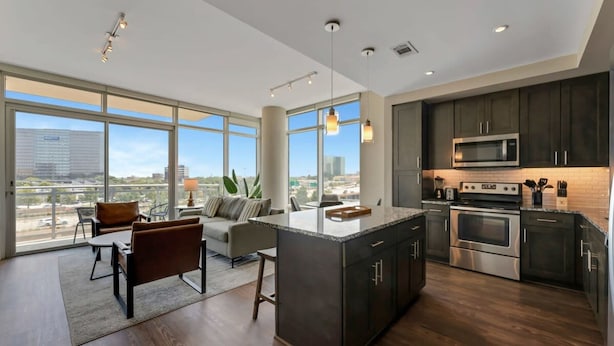 A modern kitchen with dark cabinetry, stainless steel appliances, and a large island.