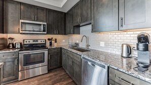 A modern kitchen with stainless steel appliances, dark cabinetry, and a granite countertop.