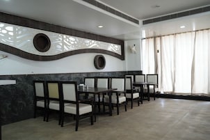 Um restaurante com interior moderno, apresentando uma parede curva com detalhes decorativos, uma fileira de mesas e cadeiras, e um grande janela com cortinas.