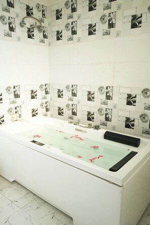 Une salle de bain dotée d’une grande baignoire, de murs recouverts de carreaux aux motifs floraux et d’un sol en marbre.