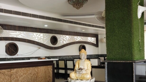 A modern interior with a Buddha statue on a lotus base, a ceiling with a unique design, and a green wall feature.