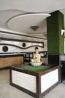 Um interior moderno com uma estátua de Buda sobre um pedestal de lótus, teto com design único e parede verde decorativa.