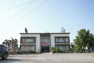 Um edifício de dois andares com uma placa indicando 'Haveli' e uma placa de 'Festa Particular'. Há uma estrutura de playground à esquerda e uma árvore à direita.