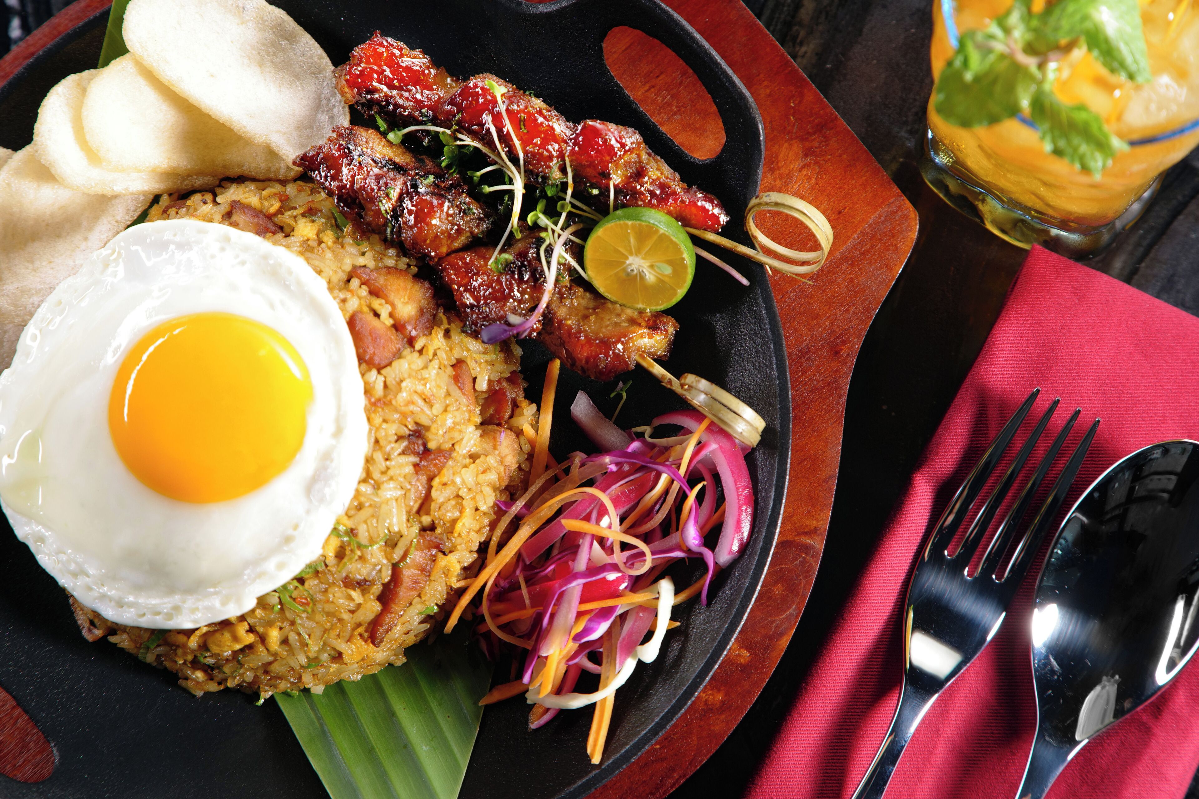A plate of food with a fried egg, skewers, and a glass of drink.
