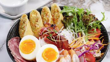 A bowl of food with various ingredients and two small bowls of sauce.