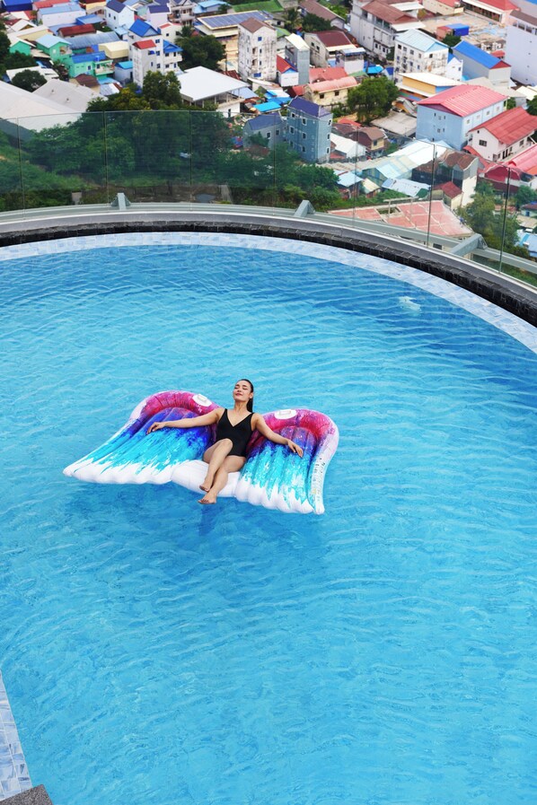 A person floating on a colorful inflatable in a swimming pool with a view of a residential area in the background. - TRIMULIA Hotel (Sihanoukville)