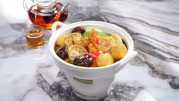 A bowl of soup with various ingredients, a teapot, and a cup of tea on a marble surface.