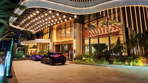 A modern hotel entrance with two cars parked in front, a curved roof design, and a well-lit facade. - TRIMULIA Hotel (Sihanoukville)