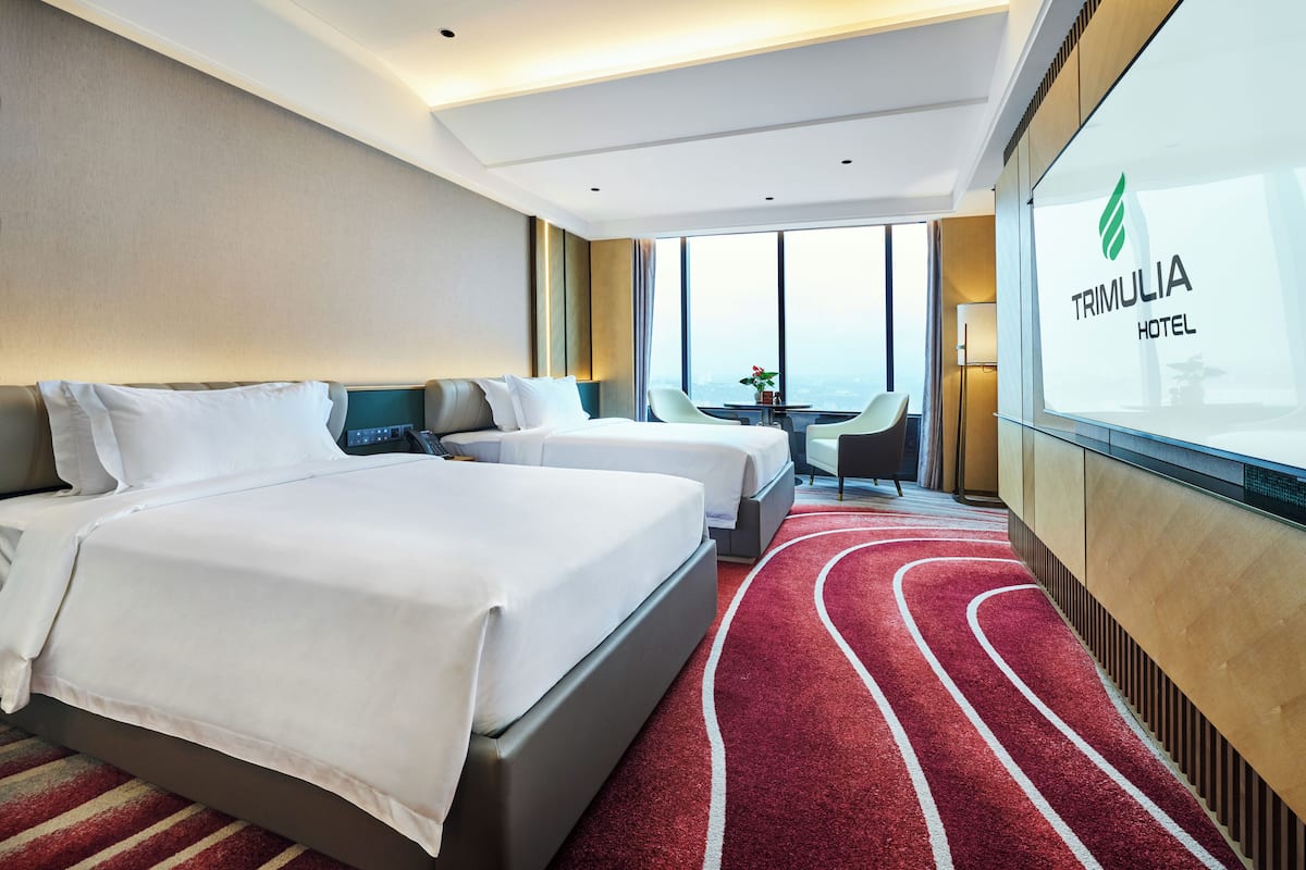 A hotel room with two beds, a red carpet, a view of the city, and a glass wall with the hotel name.