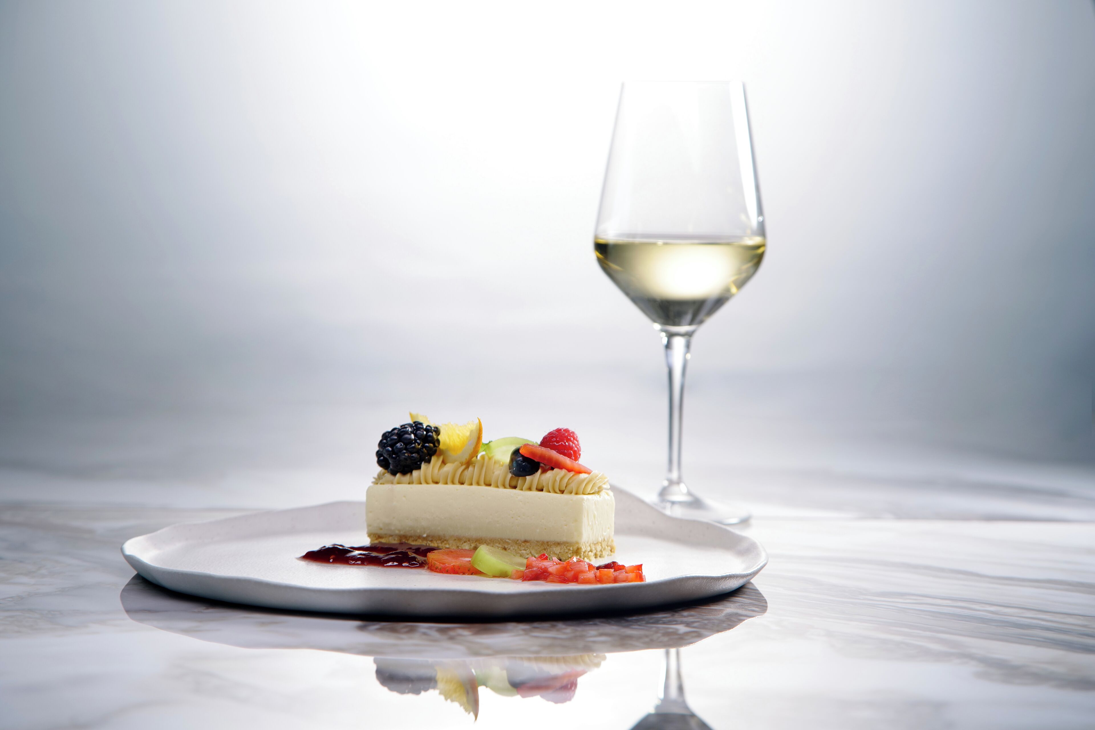 Un postre en un plato, con una copa de vino blanco a su lado.