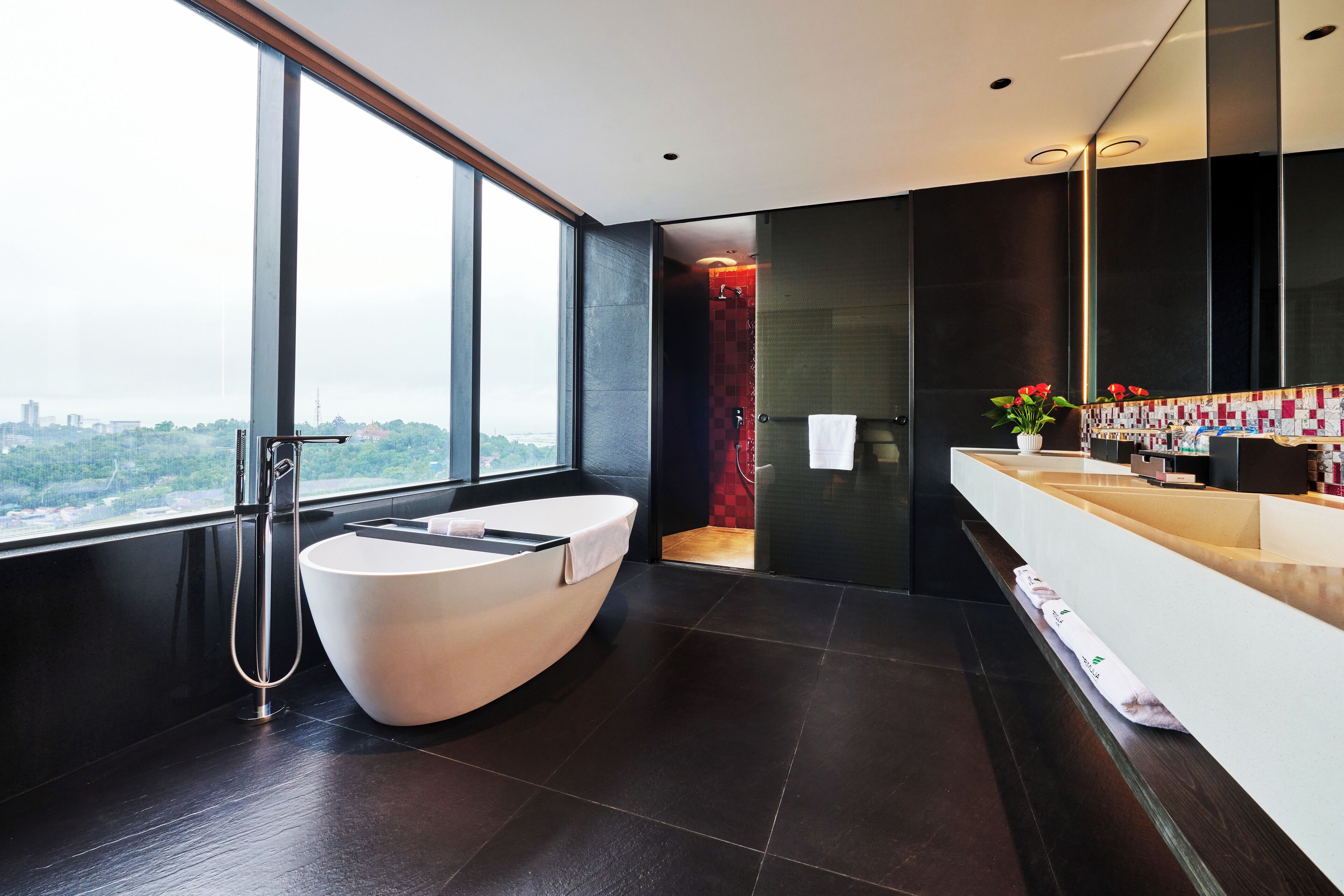 A modern bathroom with a large bathtub, a glass-enclosed shower, and a large window offering a city view.