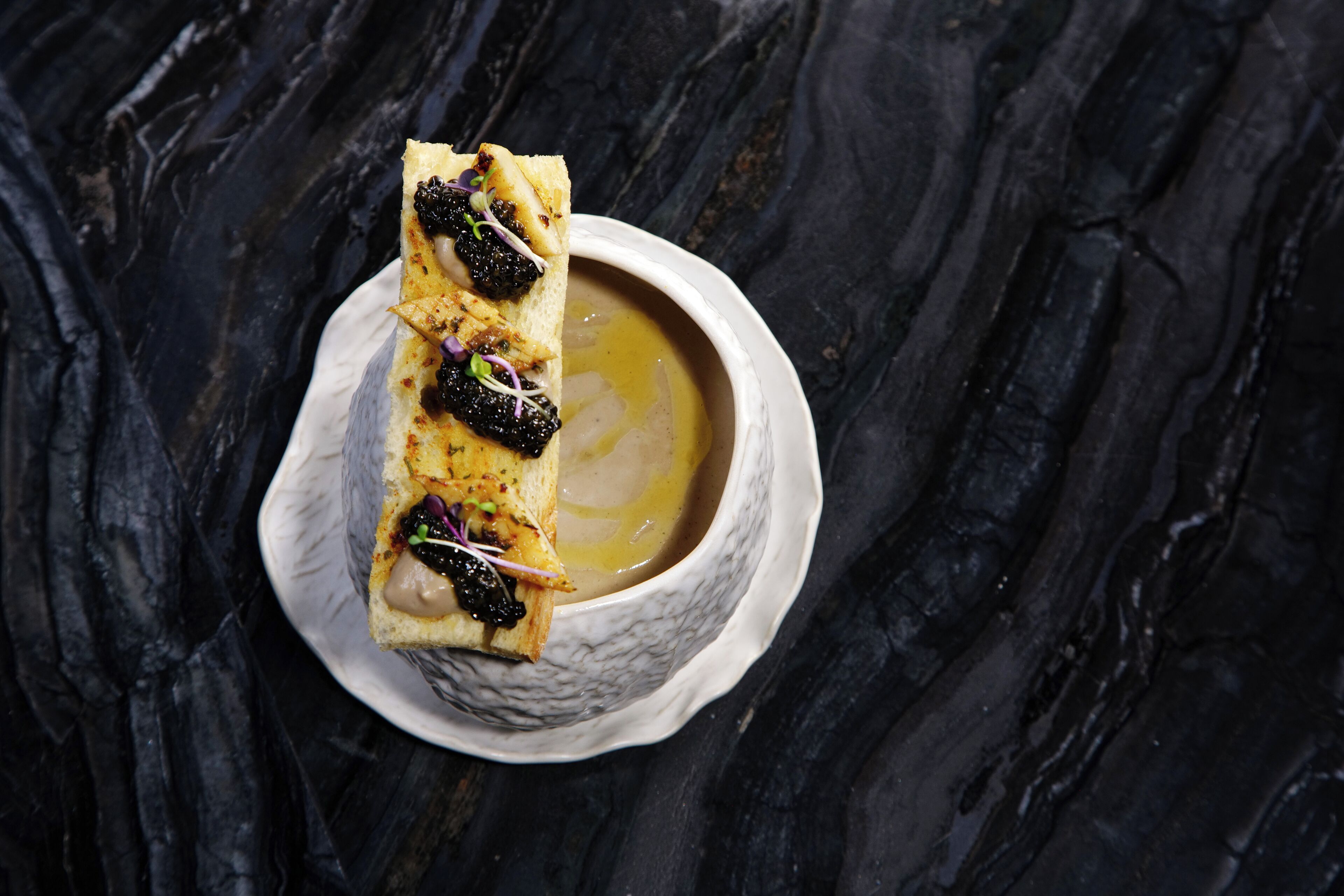 A dessert with a creamy sauce in a white bowl on a dark marble surface.
