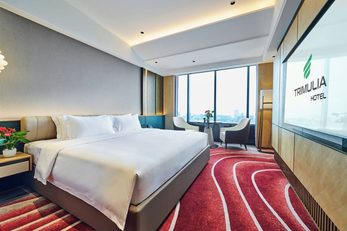 A modern hotel room with a large bed, a desk, and a view of the city.