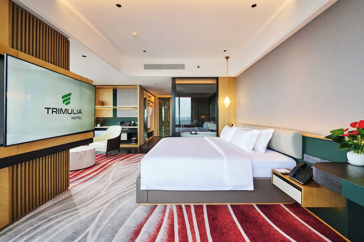 A modern hotel room with a large bed, a desk, a chair, and a TV displaying the hotel name.
