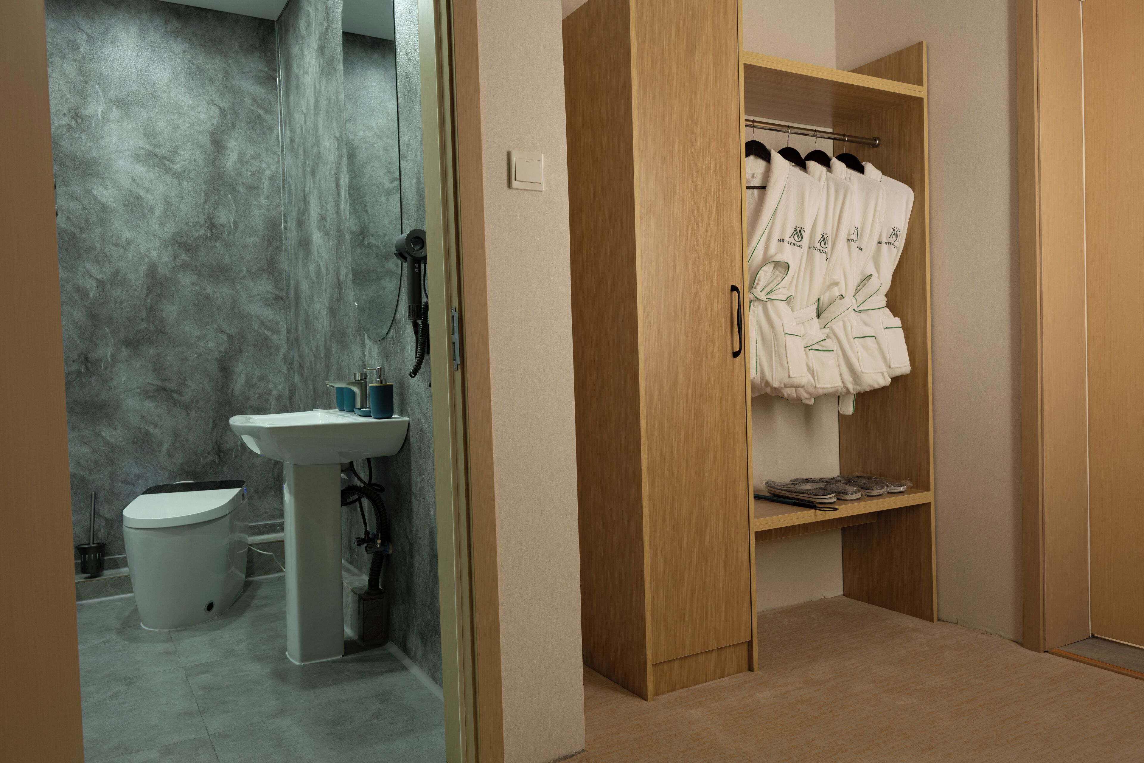 Un bagno con lavandino, WC e cabina doccia. È presente un armadio in legno con accappatoi su un appendiabiti.