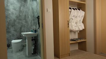 Un bagno con lavandino, WC e cabina doccia. È presente un armadio in legno con accappatoi su un appendiabiti.