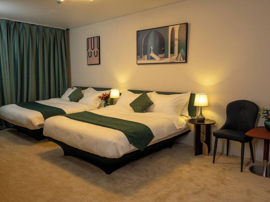 Habitación de hotel con dos camas, una silla, una mesita y un cuadro en la pared.