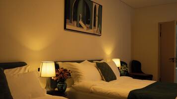 Une chambre d’hôtel avec deux lits, un tableau au mur, un vase avec des fleurs et une porte sur la droite.