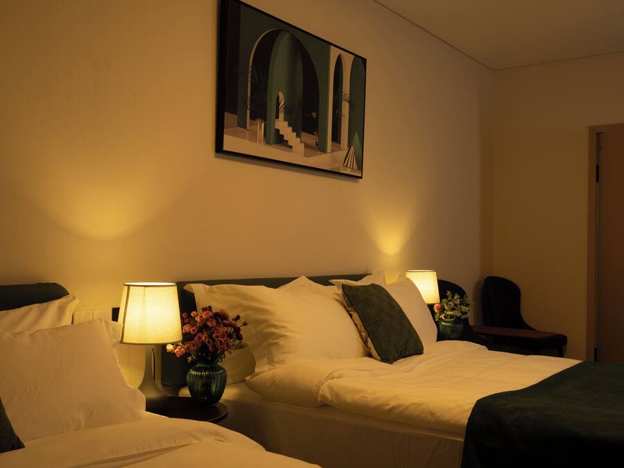 Une chambre d’hôtel avec deux lits, un tableau au mur, un vase avec des fleurs et une porte sur la droite.