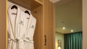 A hotel room with a wooden wardrobe containing robes, a small table with a lamp, a chair, and a sofa. - MSInternational Hotel (Ulaanbaatar)