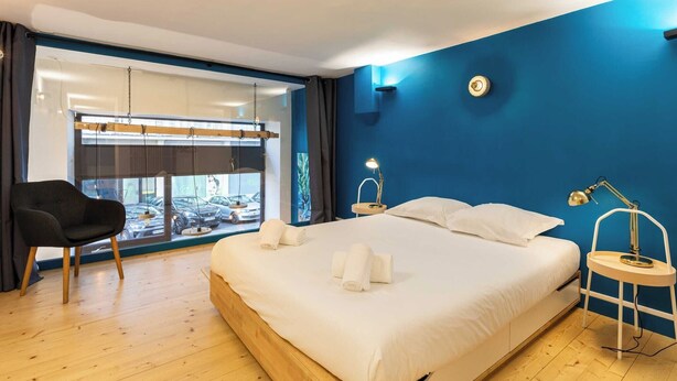 Une chambre d’hôtel moderne, dotée d’un grand lit, d’une chaise, d’un bureau et offrant une vue sur les voitures garées à travers une grande fenêtre.