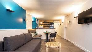 Un salon moderne avec un canapé gris, une table en osier et un coin cuisine à l’arrière-plan.