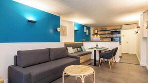 Un salon moderne avec un canapé gris, une table ronde en osier et un coin cuisine comprenant une table à manger et des chaises.