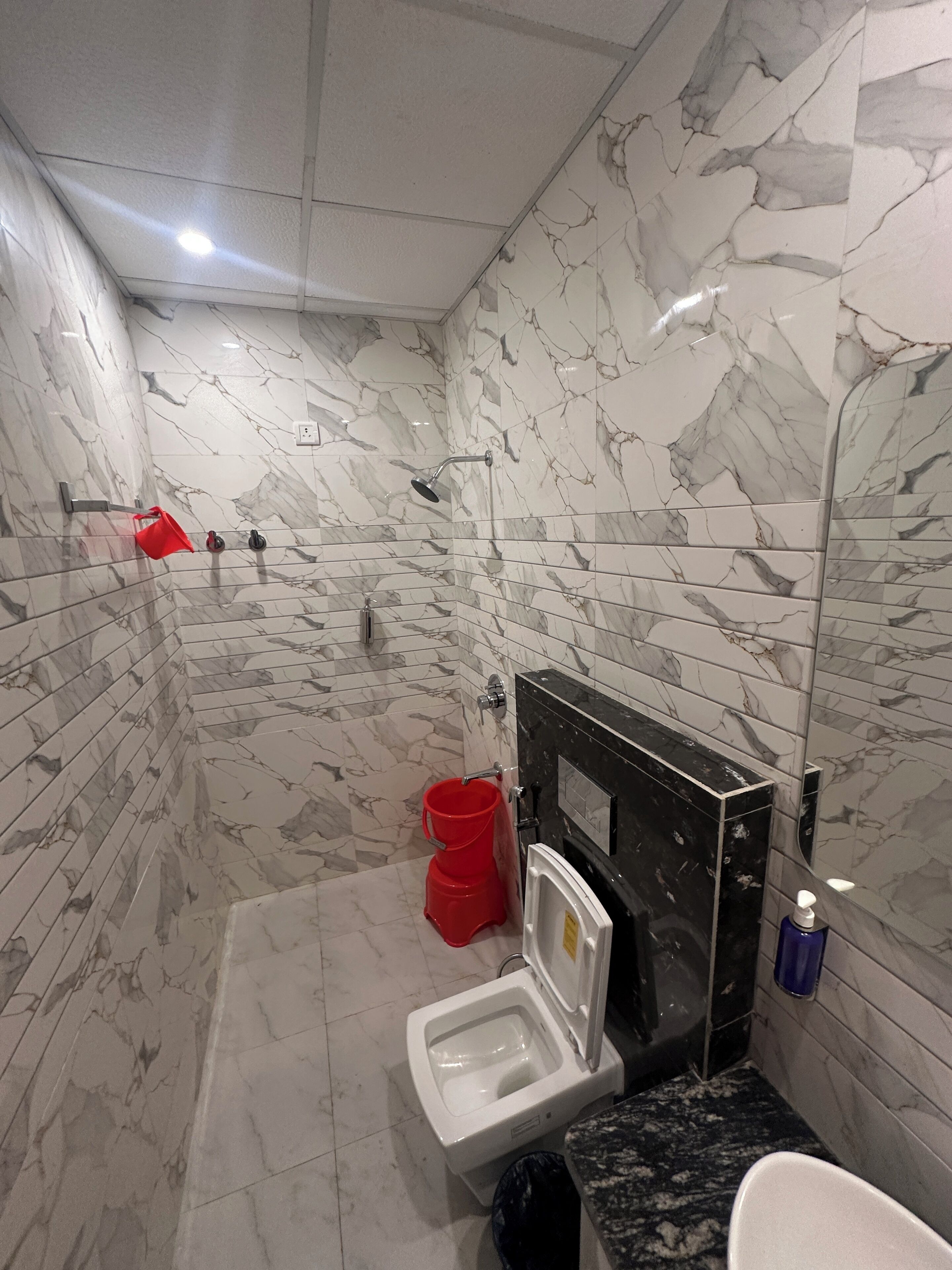 A bathroom with marble walls, a shower, a toilet, and a sink.