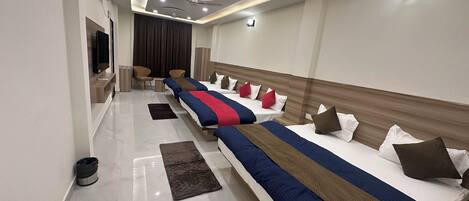 A hotel room with three beds, a flat-screen TV, a ceiling fan, and a modern light fixture.