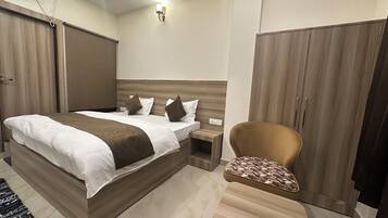 Una habitación de hotel moderna con una cama grande, un armario de madera, una mesita de noche pequeña y un sillón con estampado.