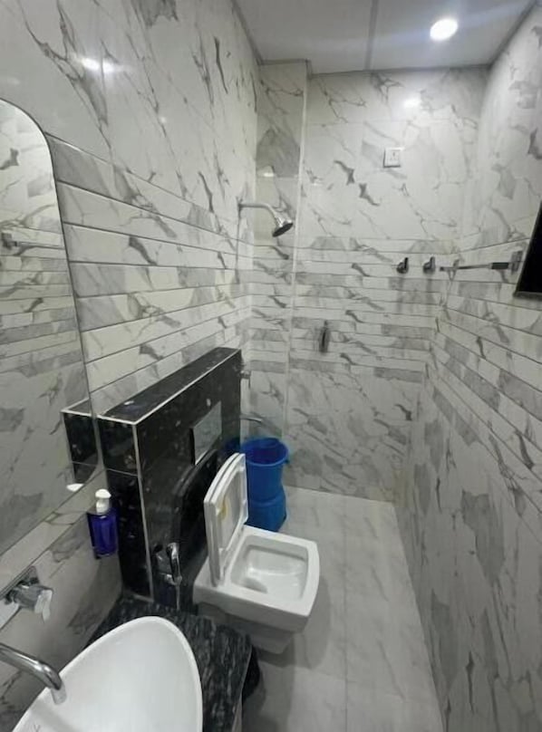 Egy márványburkolatú fürdőszoba, amelyben mosdókagyló, WC és zuhanyzó található.
