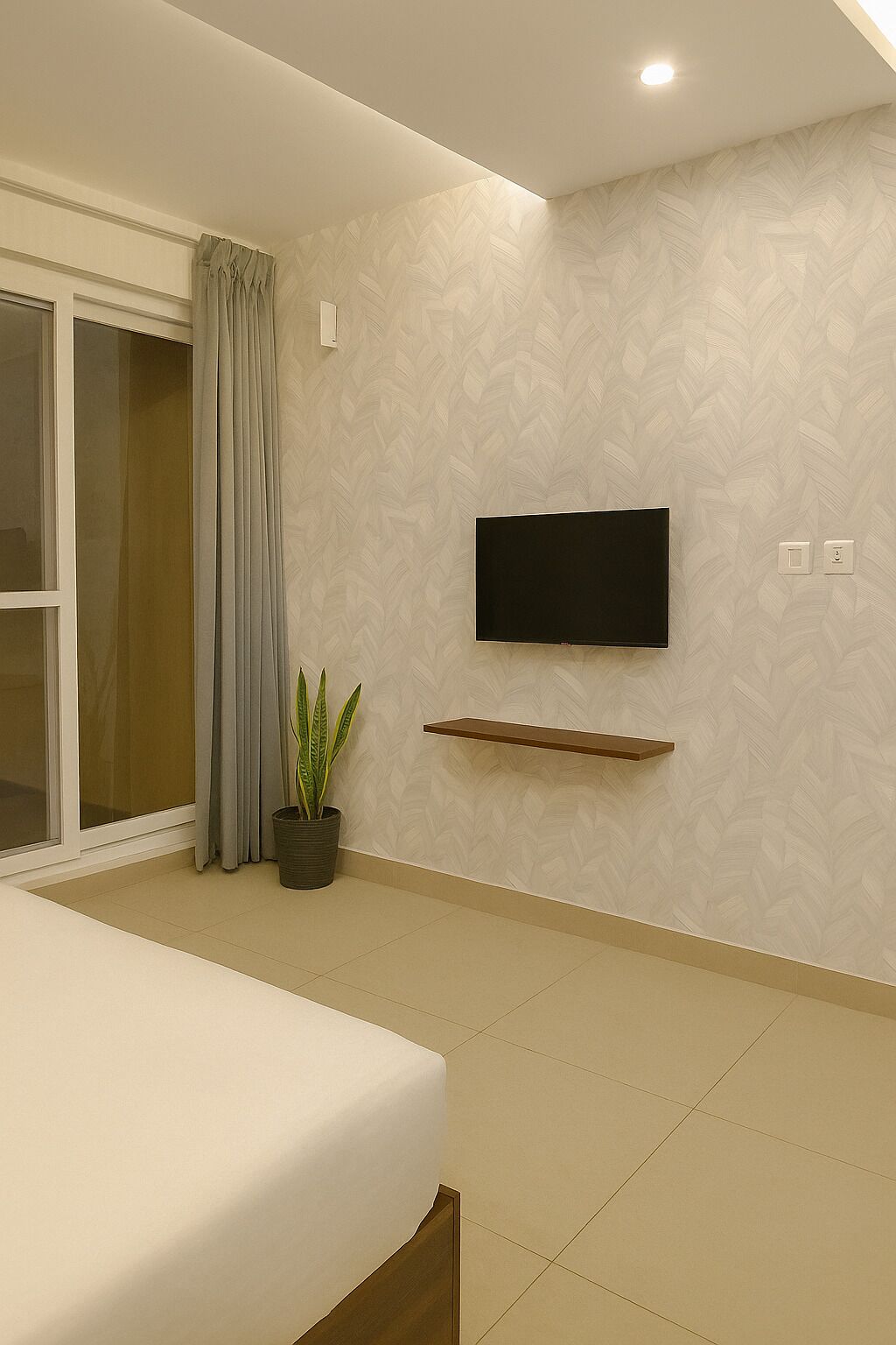 Un dormitorio con una cama, una planta en maceta, un televisor montado en la pared y un ventanal corredero.