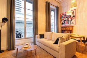 A cozy living room with a sofa, a small table with a glass of wine, and a dining table set for two.