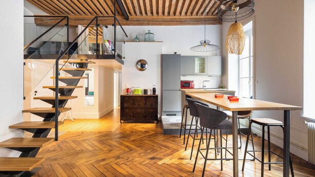 A modern kitchen with a wooden staircase, a dining area with bar stools, and a large window providing natural light. - DIFY Roi Lyon - Hotel de Ville (Lyon)