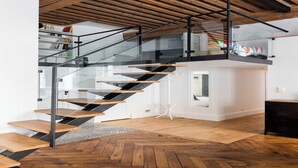 A modern staircase with glass railings and wooden steps, leading to a loft area with a white wall and a small white table. - DIFY Roi Lyon - Hotel de Ville (Lyon)