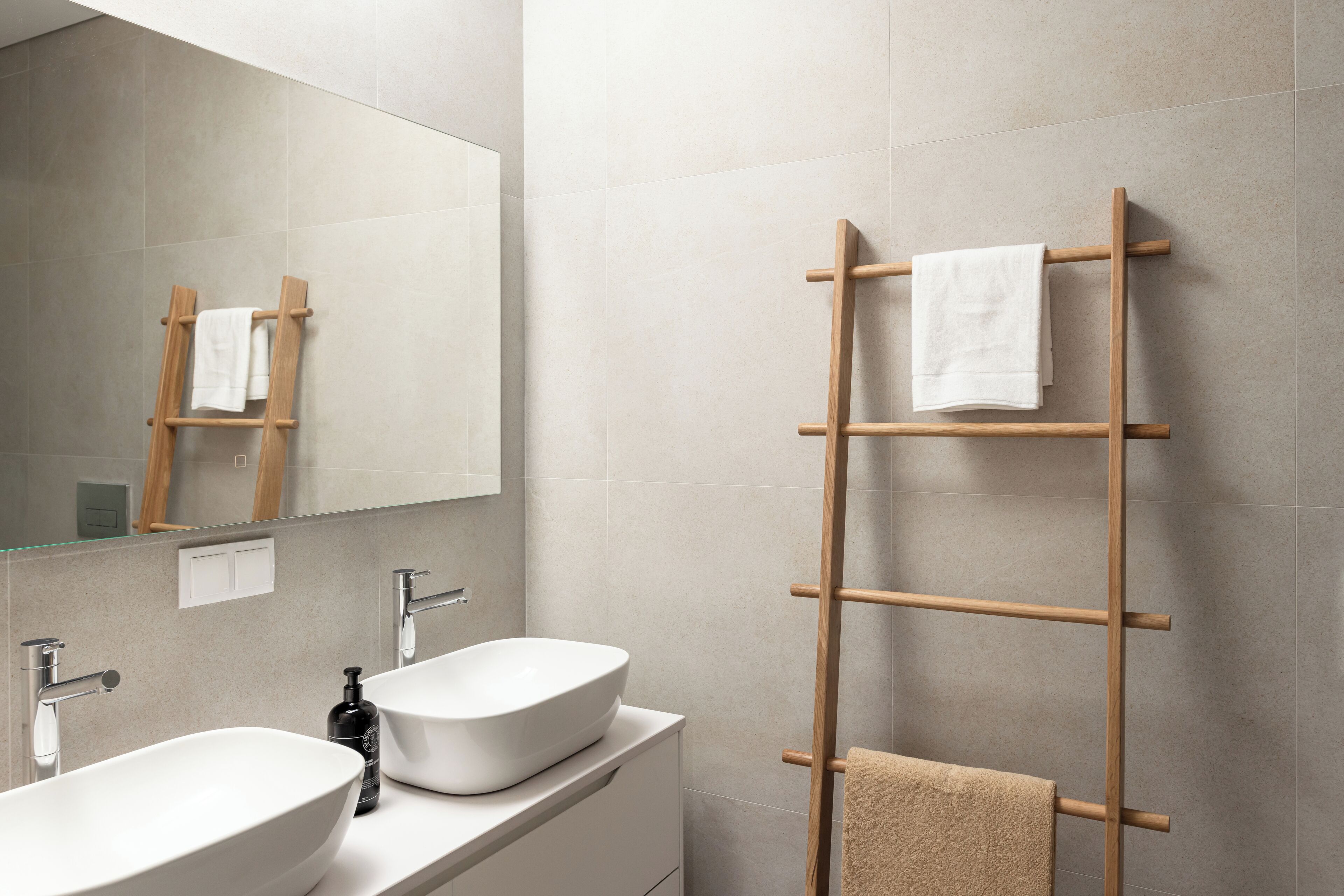 A modern bathroom with two sinks, a wooden towel rack, and a mirror.