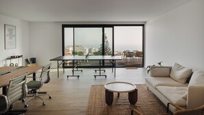 Un salon moderne avec une grande table, deux chaises, un canapé et une vue sur la ville grâce à de grandes fenêtres.